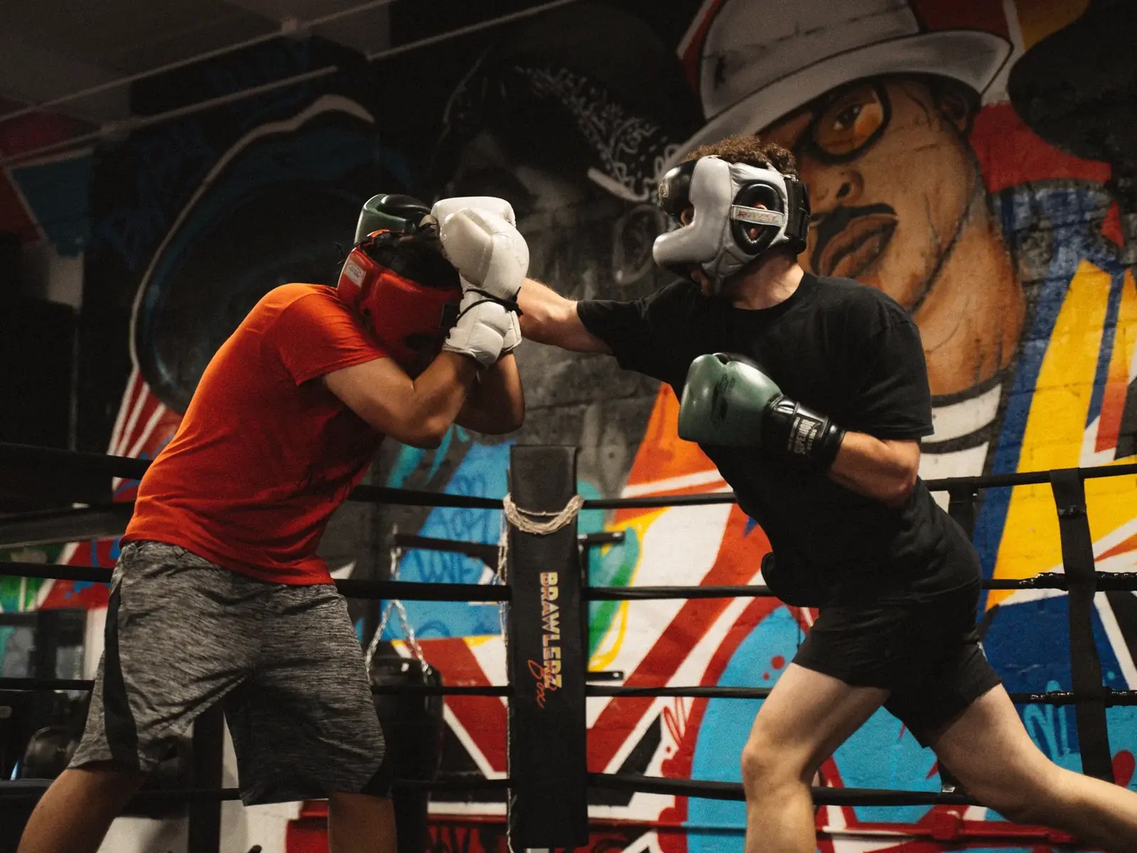 Two fighters sparring in headgear in front of a graffiti mural