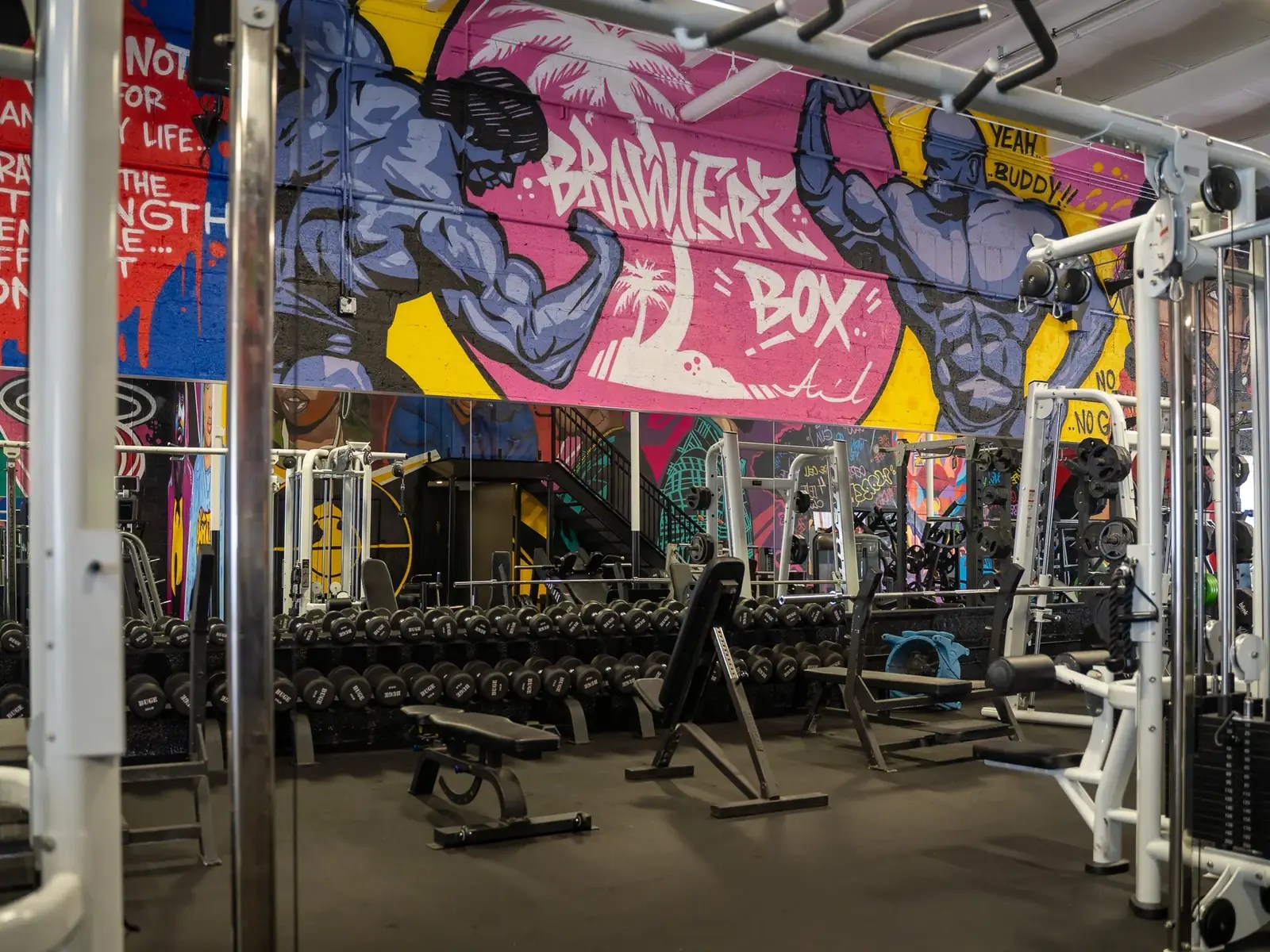 Weight room with dumbbell racks under a pink Brawlerz Box mural