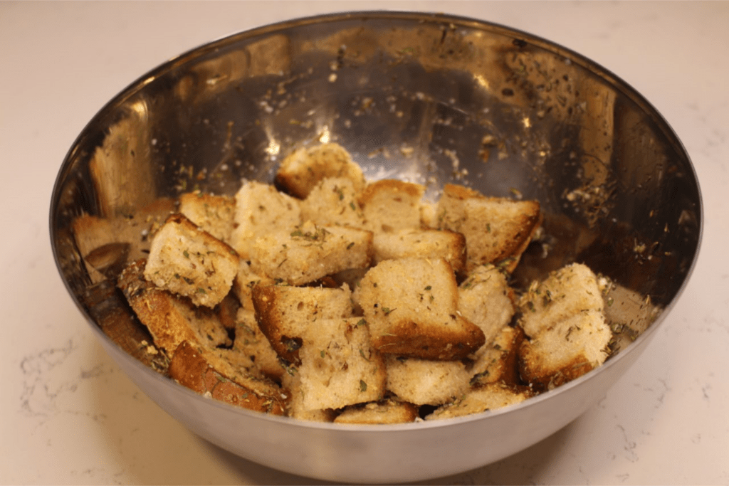 Medium sized metal bowl with bread pieces coated with olive oil and seasonings