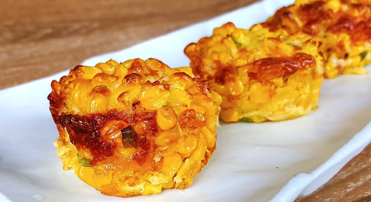 Three golden-brown corn fritters served on a white plate