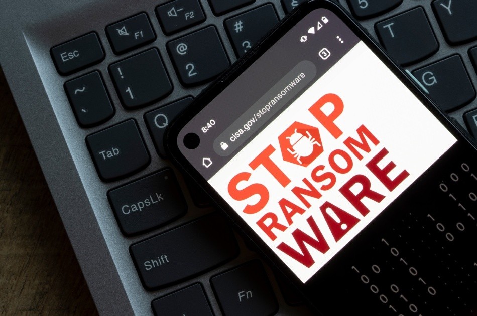 Phone screen lying on top of a laptop keyboard. The screen shows a browser open at "cisa.gov/stopransomware" and the Stop Ransomware logo