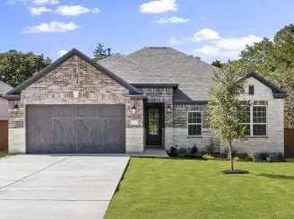 Front view of a modern single-family home with a stone and brick facade, a two-car garage, a well-manicured lawn, and a small tree in the yard against a blue sky.