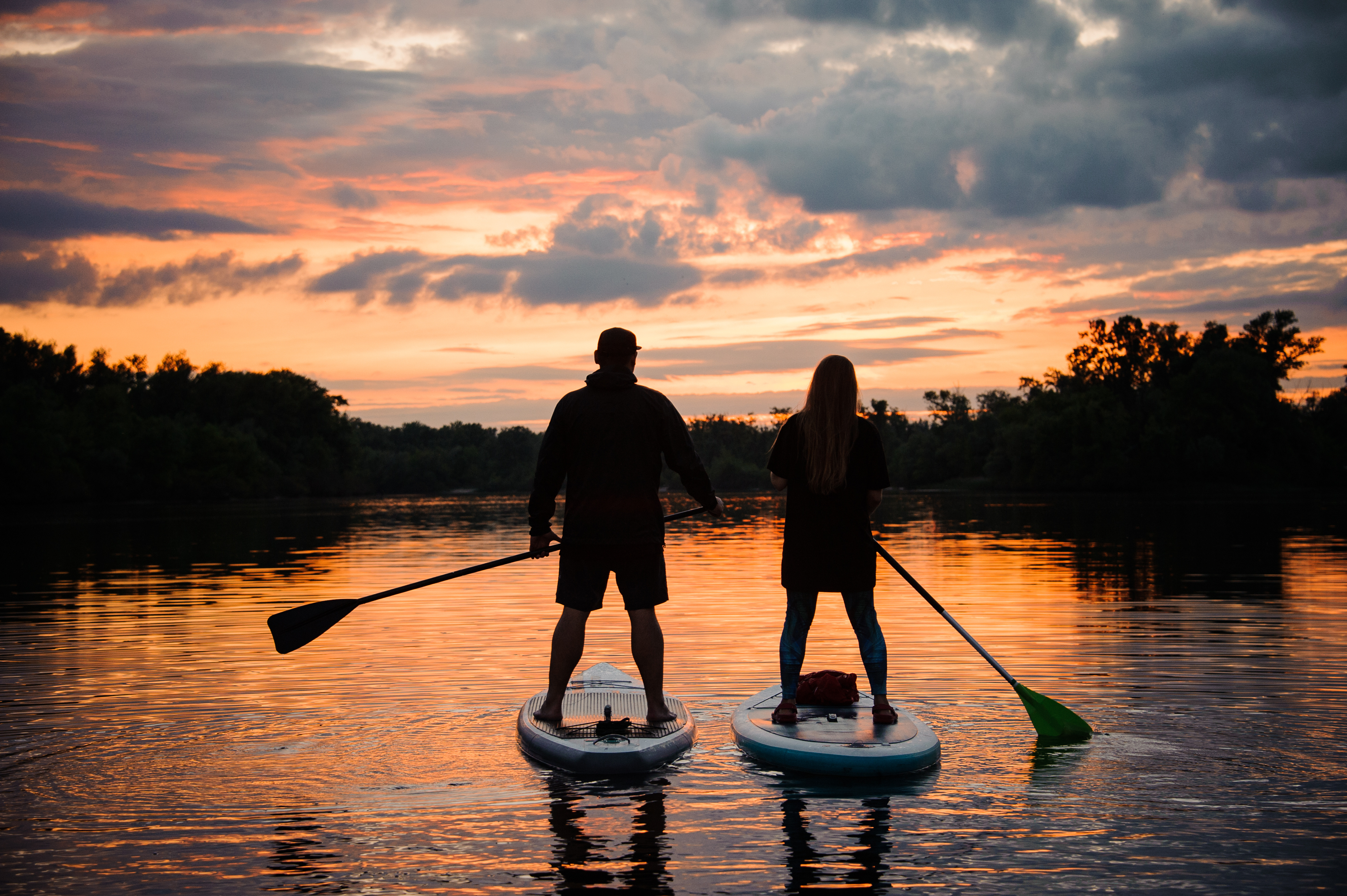 A couple standing on paddle boards, floating down the river at sunset in Brevard, NC.
