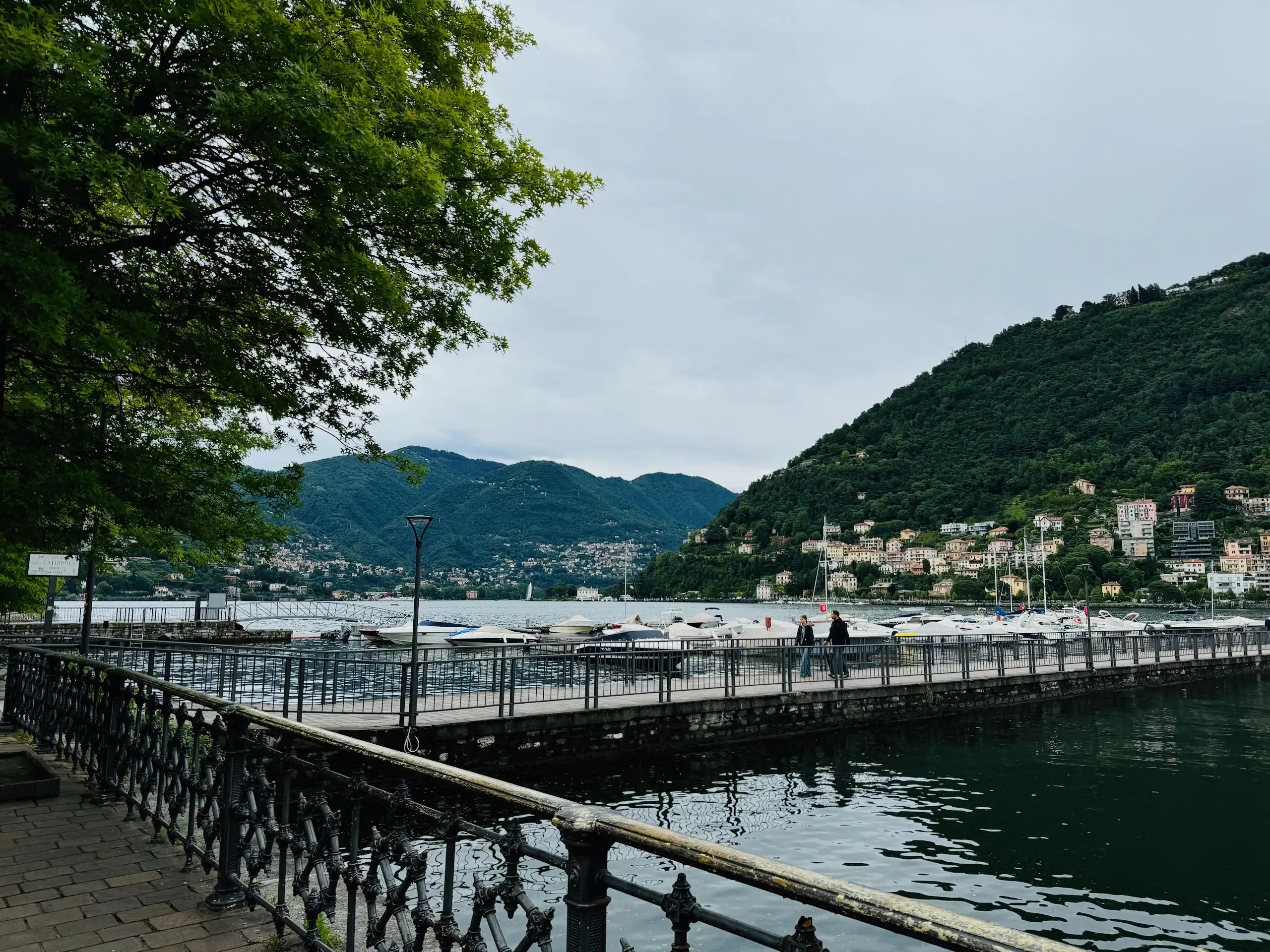 Como Gölü kenarında yürüyüş yolu, doğa ve şehir manzarası.