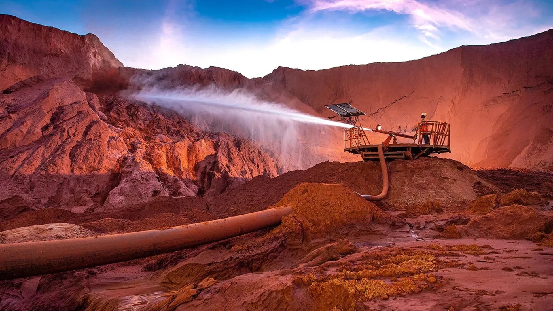 Water spraying system operating at an open pit mine in kenya with red earth terrain and mining equipment visible at dusk