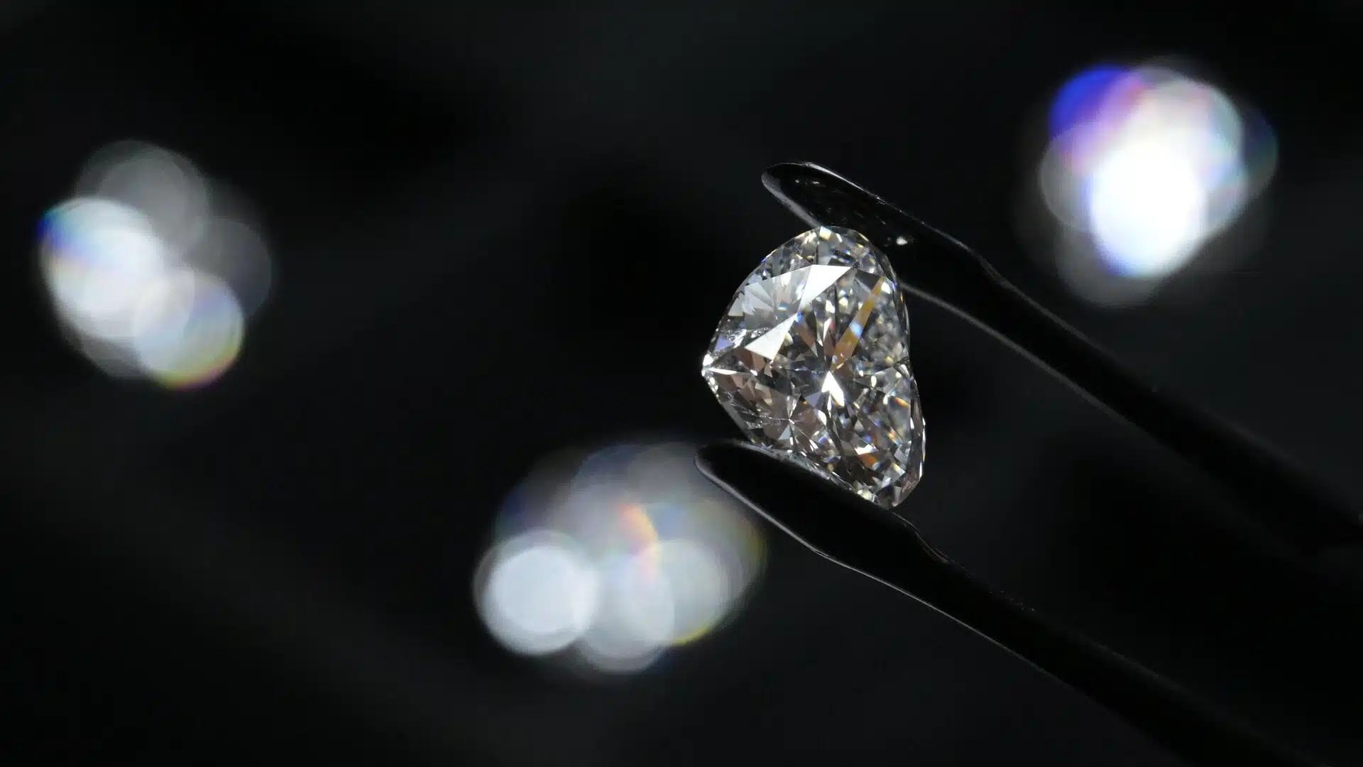 A large faceted diamond held by precision tweezers against a dark background reflecting light