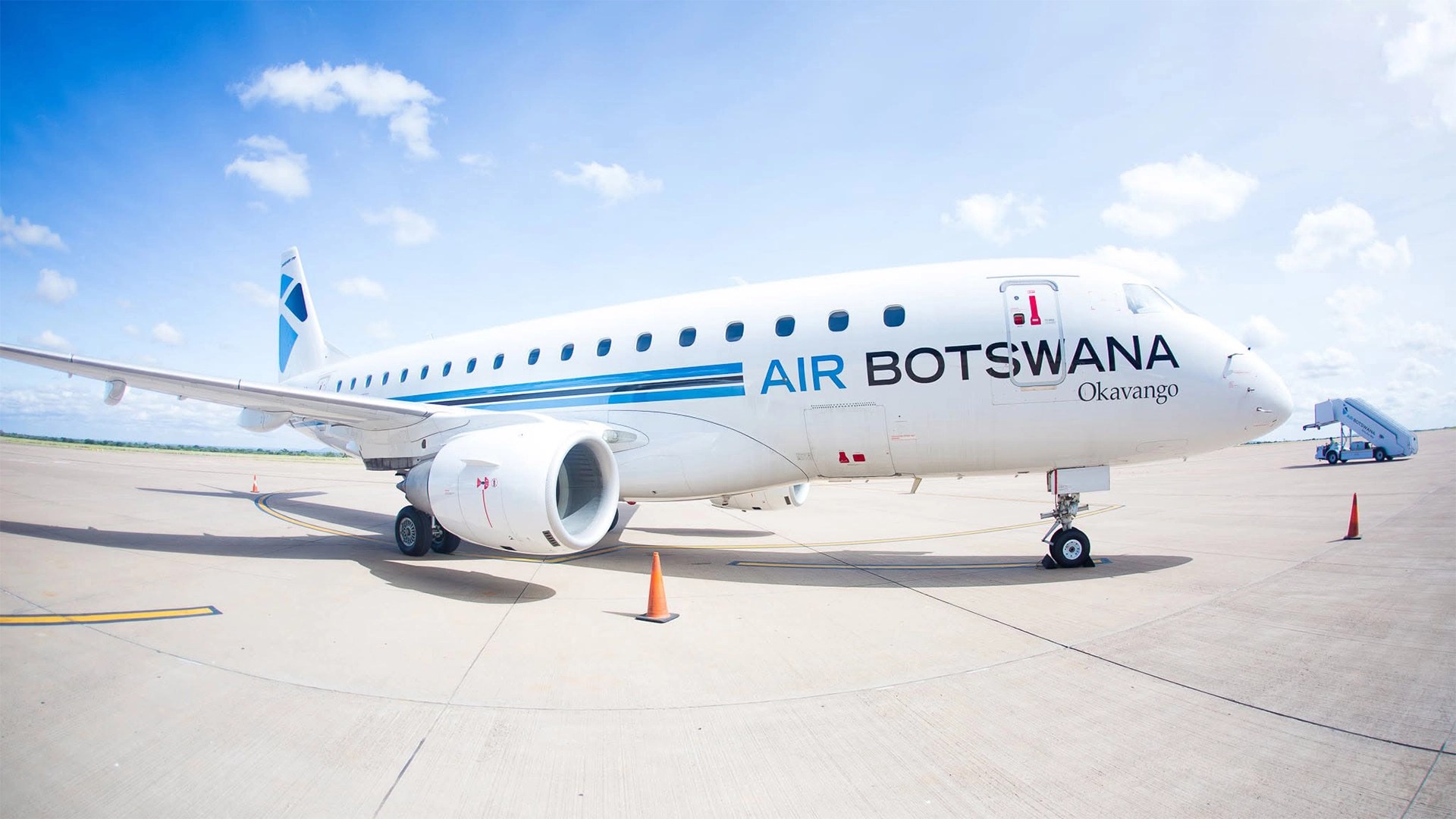 Air botswana embraer e170 jet named okavango parked on an airport apron under a blue sky displaying the airlines blue and white livery