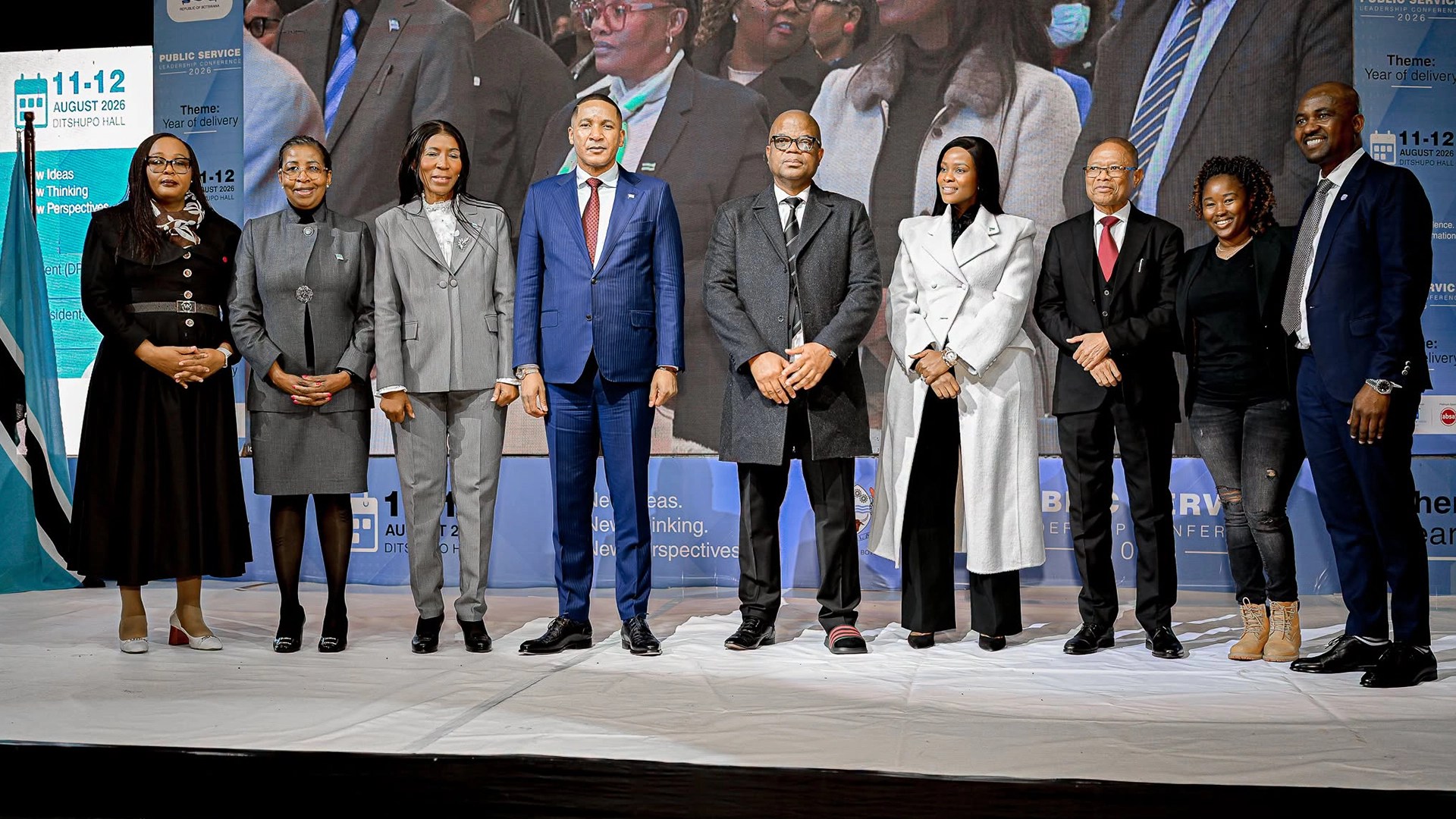 Botswana government leaders and senior public sector officials stand on stage at the 2026 public service leadership conference at ditshupo hall with event branding and the botswana flag visible behind them