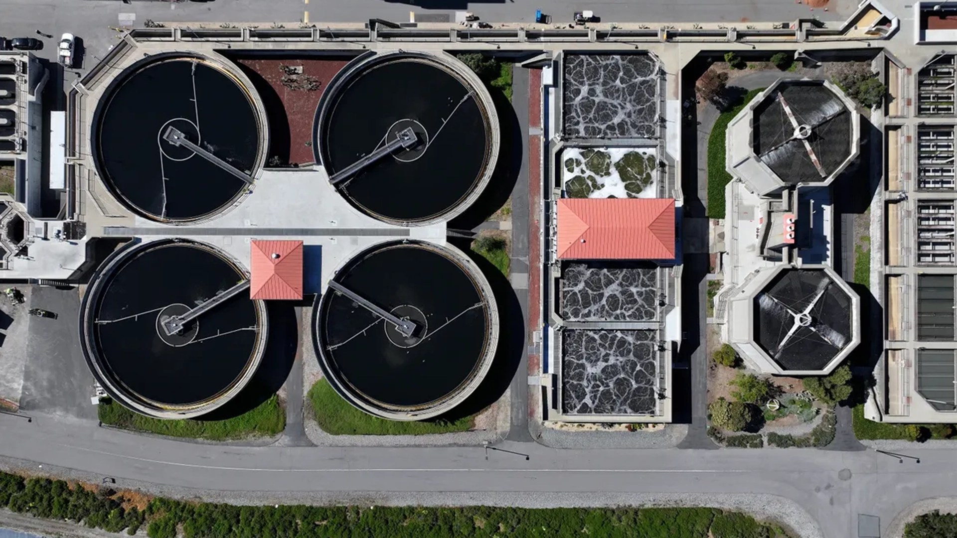 Aerial view of a wastewater treatment facility with four large circular clarifier tanks treatment basins filtration systems and surrounding industrial infrastructure