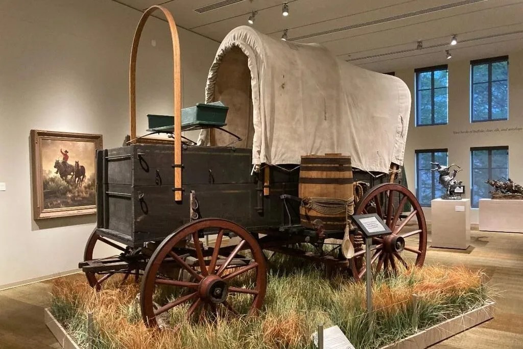 A black colored wagon on grass and a barrel tied to it's side.