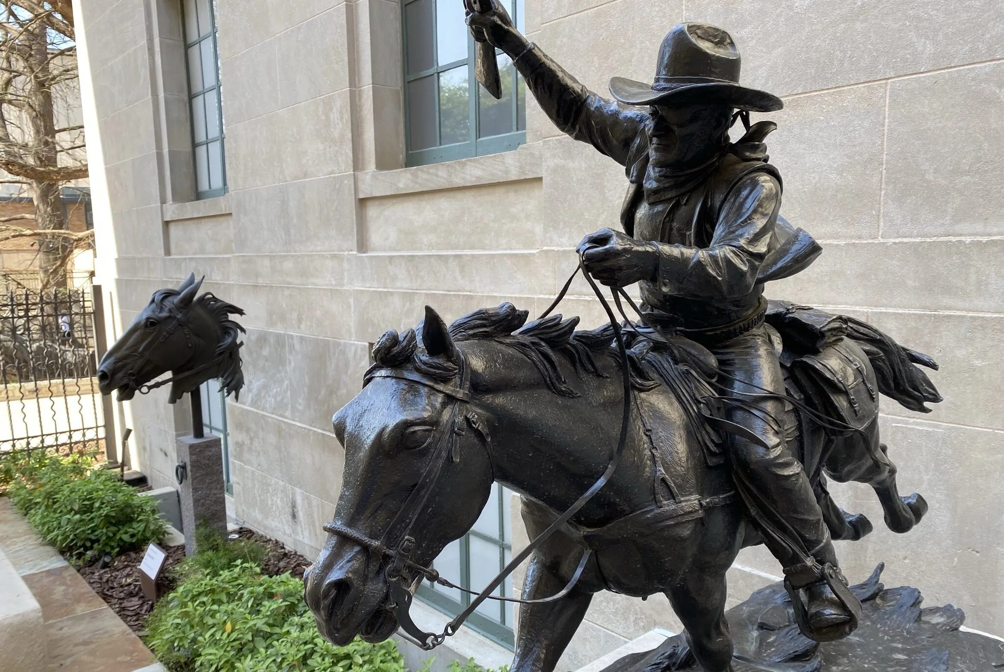 A statue of a cowboy riding a horse in mid action. In the background there is also a statue of a horse's head.
