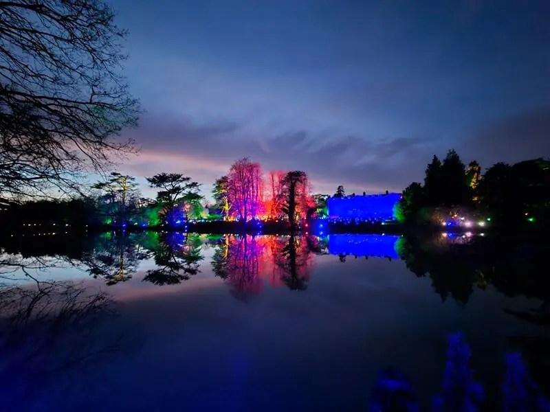 view over lake of Compton Verney hall and lit up trees reflected