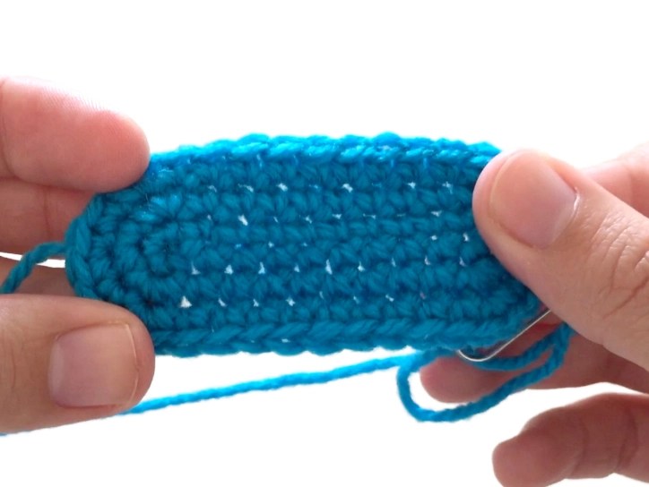 Woman's hands holding up a flat crochet piece worked around the chain