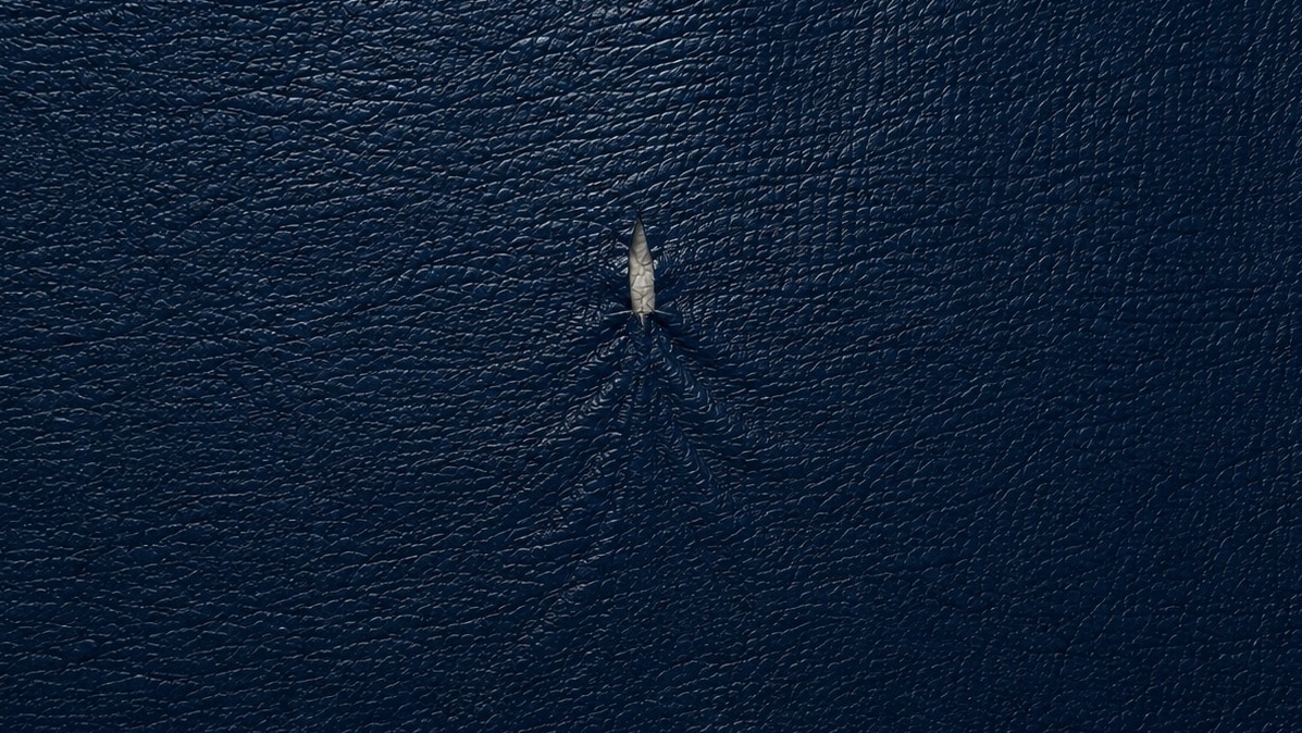 Close-up of a tear in dark blue fabric that resembles a boat and wake
