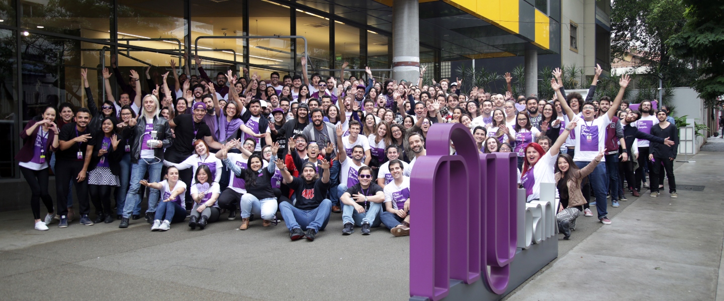 A bunch of Nubankers at the entrance of the office in Sao Paulo, Brasil, raising their hands and smiling