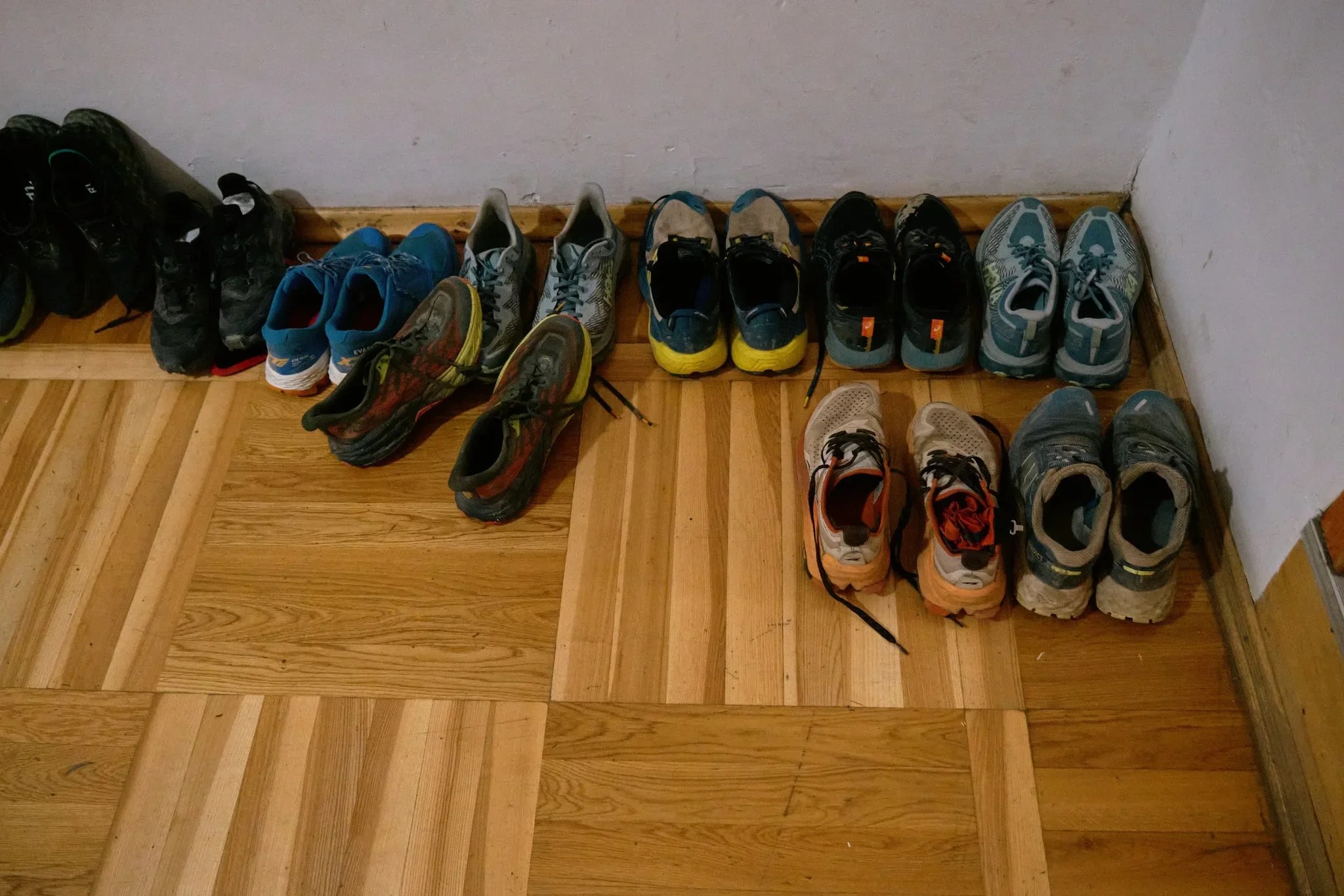 Buty sportowe i trekkingowe ustawione na podłodze przy ścianie.