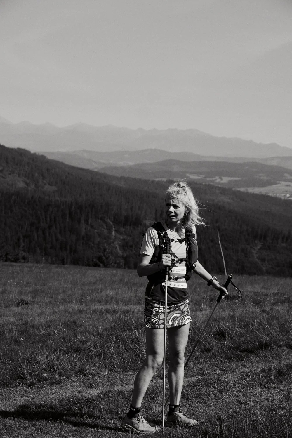 Kobieta biegająca z kijami trekkingowymi na tle górskiego krajobrazu.