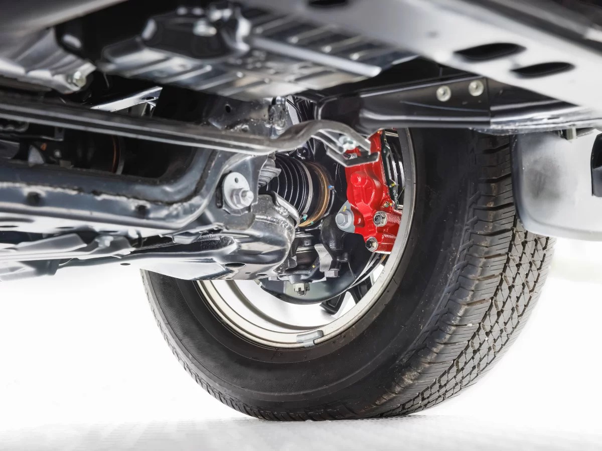 Close-up of a car's underside, showcasing the wheel, tire, and red brake caliper against a metallic frame.