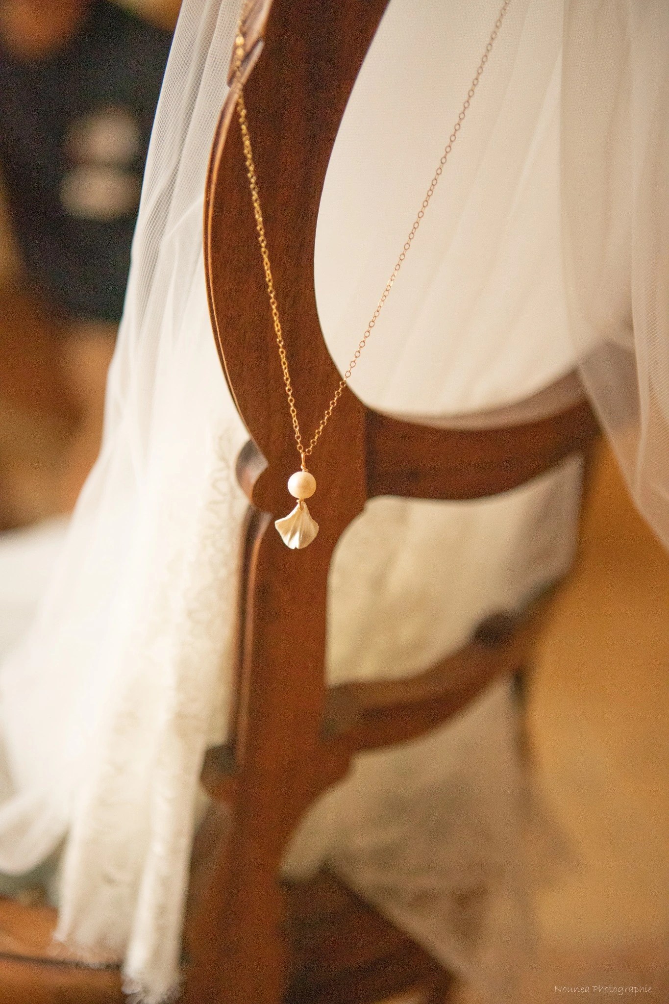 Collier mariage VIVIENNE posé sur une chaise ancienne près d'un voile, pendentif perle et pétale nacré, by Marguerite