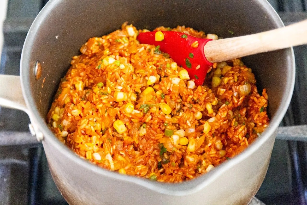 Rice being cooked in a pot with herbs corn, spices, and tomato paste