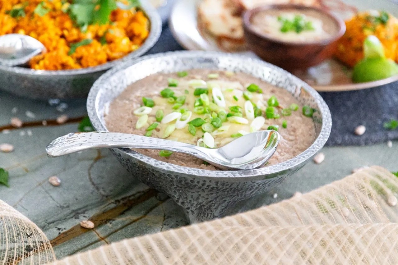 Pewter bowl of beans with Mexican Rice in the background