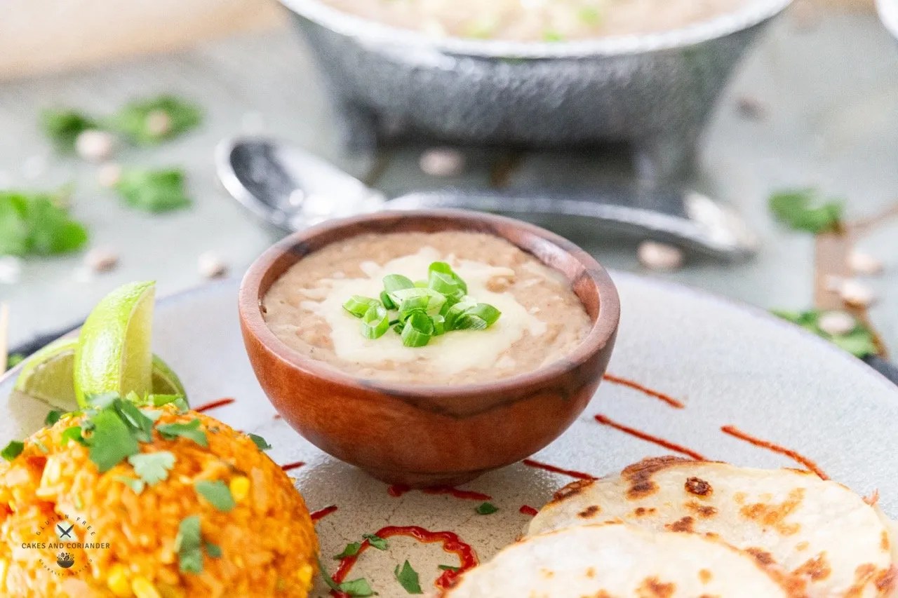 refried beans in a wooden bowl with chihuahua cheese and green onions