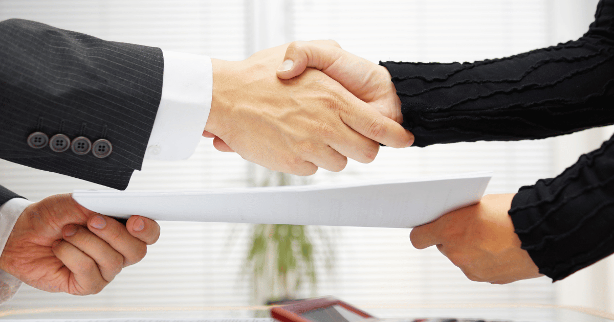 two people exchanging paperwork and shaking hands simultaneously