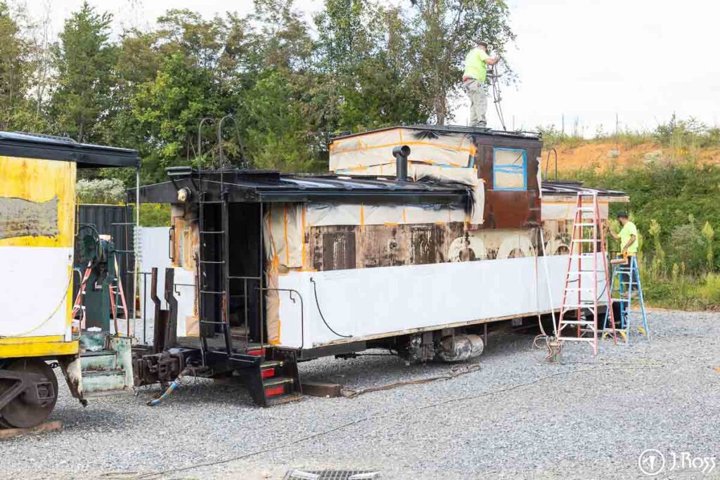 J. Ross crew applying Sher-Cryl white stripe while another team member sprays gloss black enamel on roof of caboose