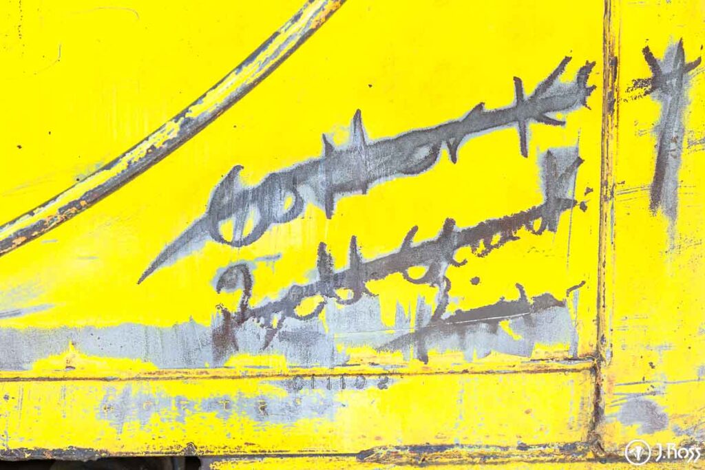 Close-up of worn yellow caboose surface showing old paint layers and markings being stripped away for restoration