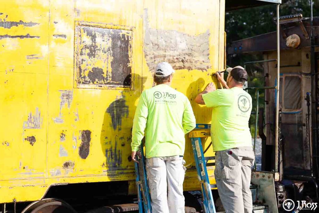 Painters measuring and marking the yellow caboose to ensure the stripe is perfectly straight