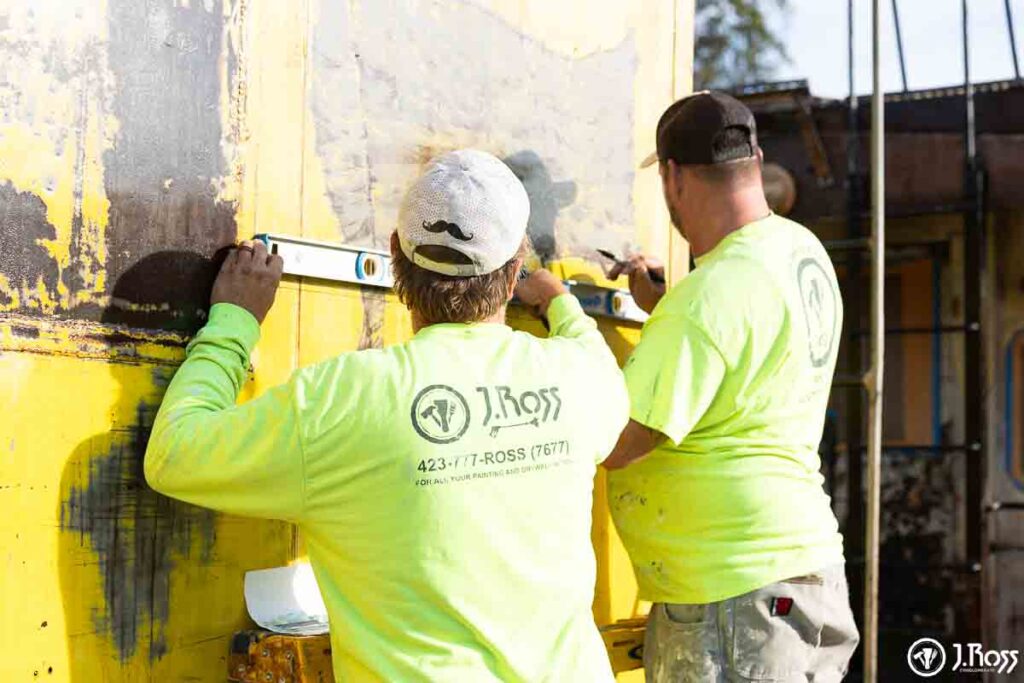 Team using a level and pencil to set guide lines for the Sher-Cryl HPA white stripe