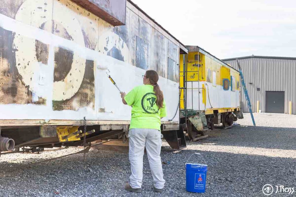 Crew member rolling Sher-Cryl HPA white paint onto the side of the caboose