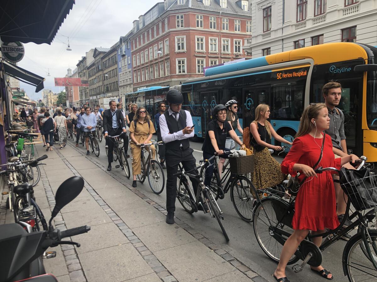 Un groupe de cyclistes dans une rue animée de Copenhague, avec des passants et des bus en arrière-plan.