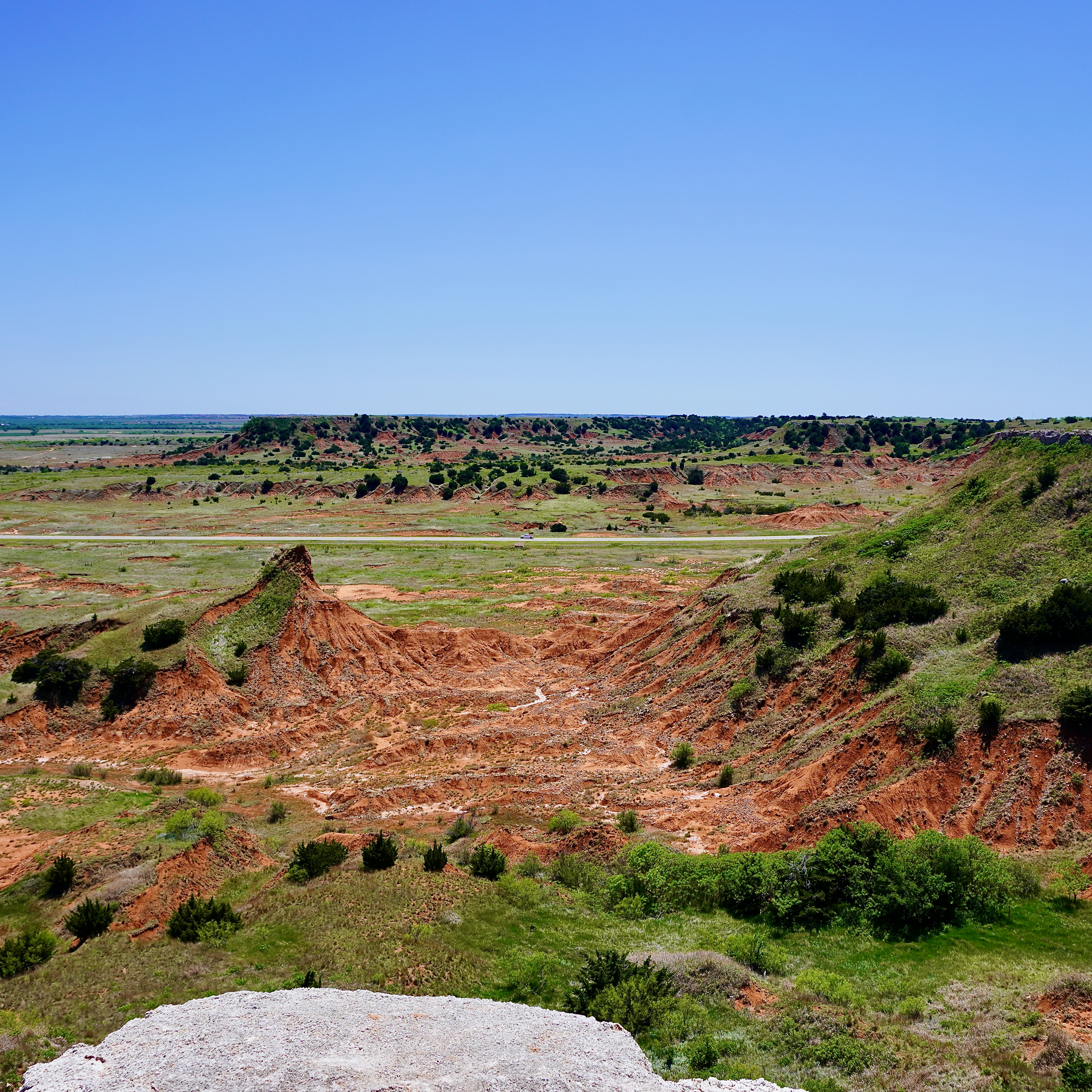 a wide view of red dirt and green grass and blue sky from a cliff edge