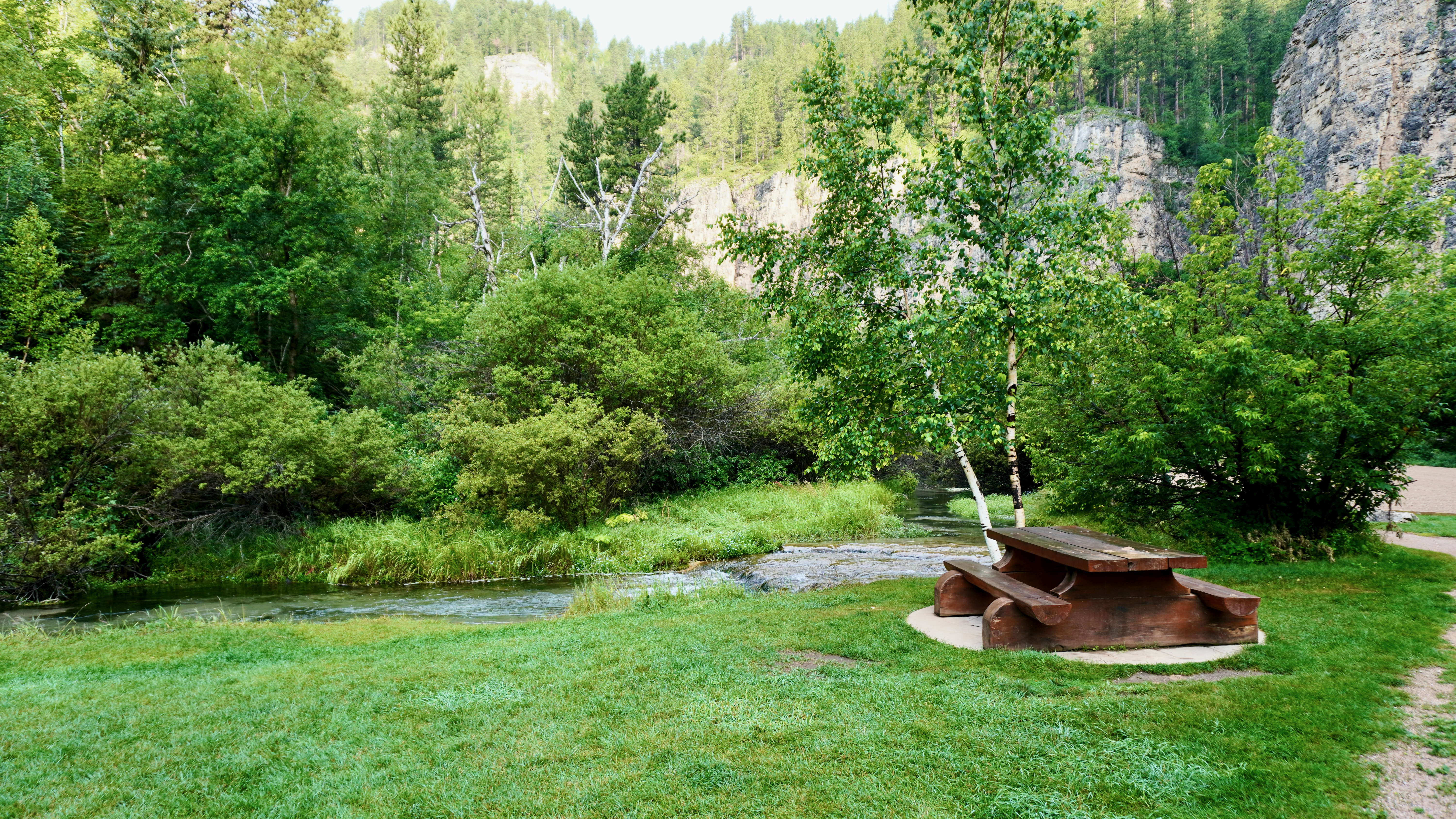 a creek flows by a picnic table with cliffs in the background
