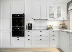 Modern kitchen with white cabinets, sleek black appliances, and wood accents, featuring a coffee maker and organized countertop.