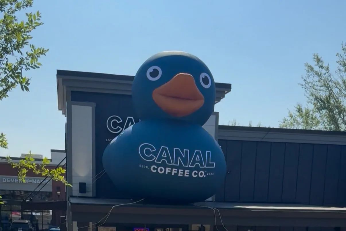 Giant blue duck mascot outside Canal Coffee Co. storefront under a clear blue sky