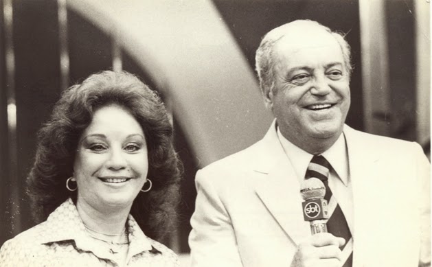 Lolita Rodrigues e seu marido Airton Rodrigues aparecem durante transmissão do programa Almoço com as Estrelas. A foto em p&B mostra ambos sorrindo com microfone na mão.