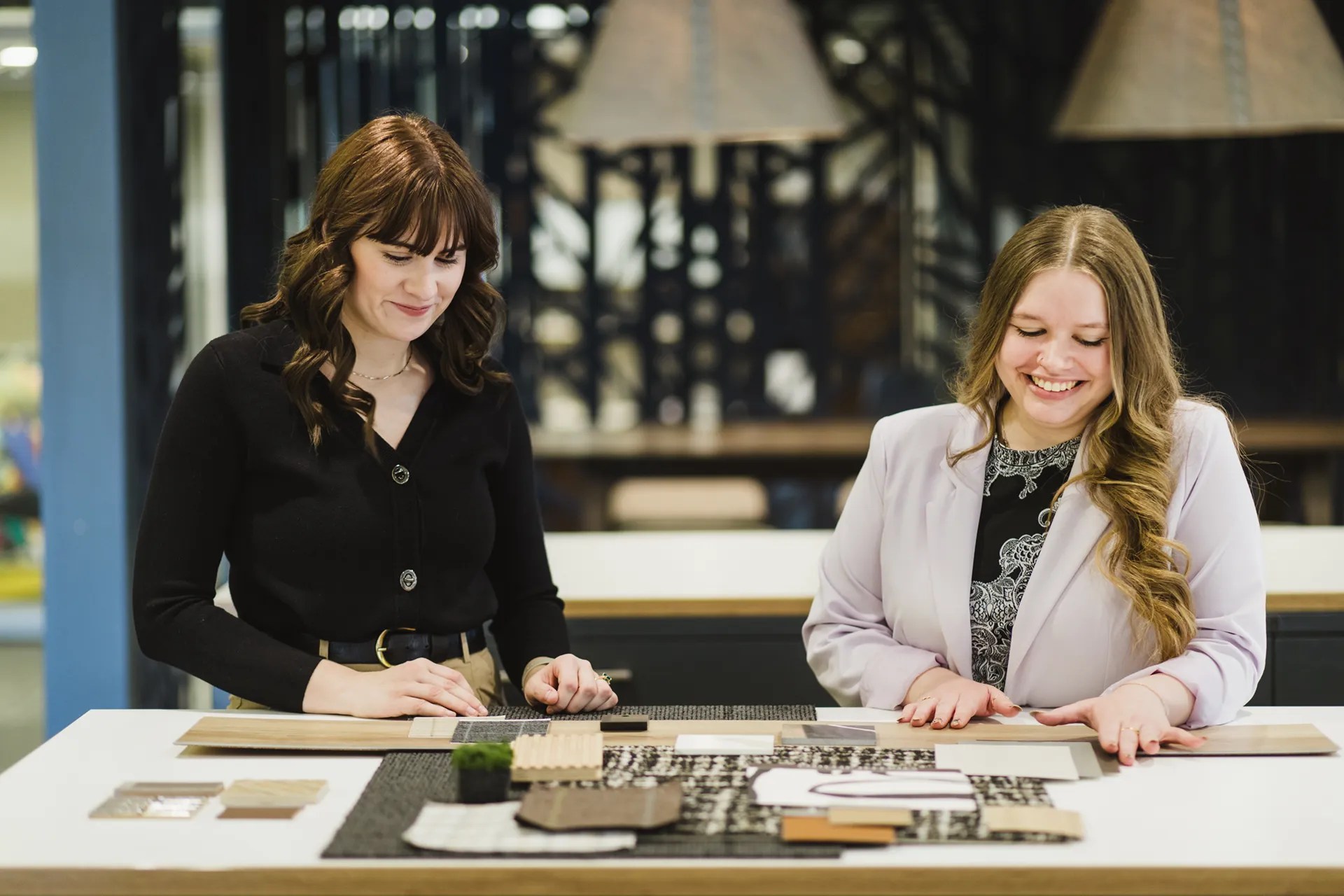 Two interior designers collaborating over material samples and design options at a table, highlighting their teamwork in finalizing project details.