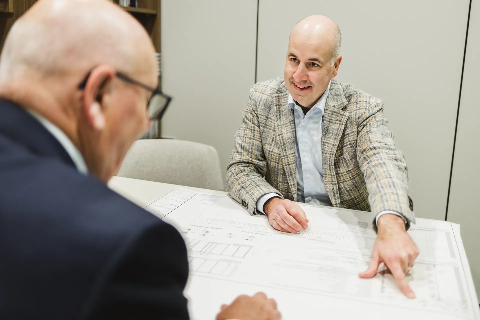 Two professionals engaged in a design consultation, analyzing architectural plans and discussing project details with focused expressions.