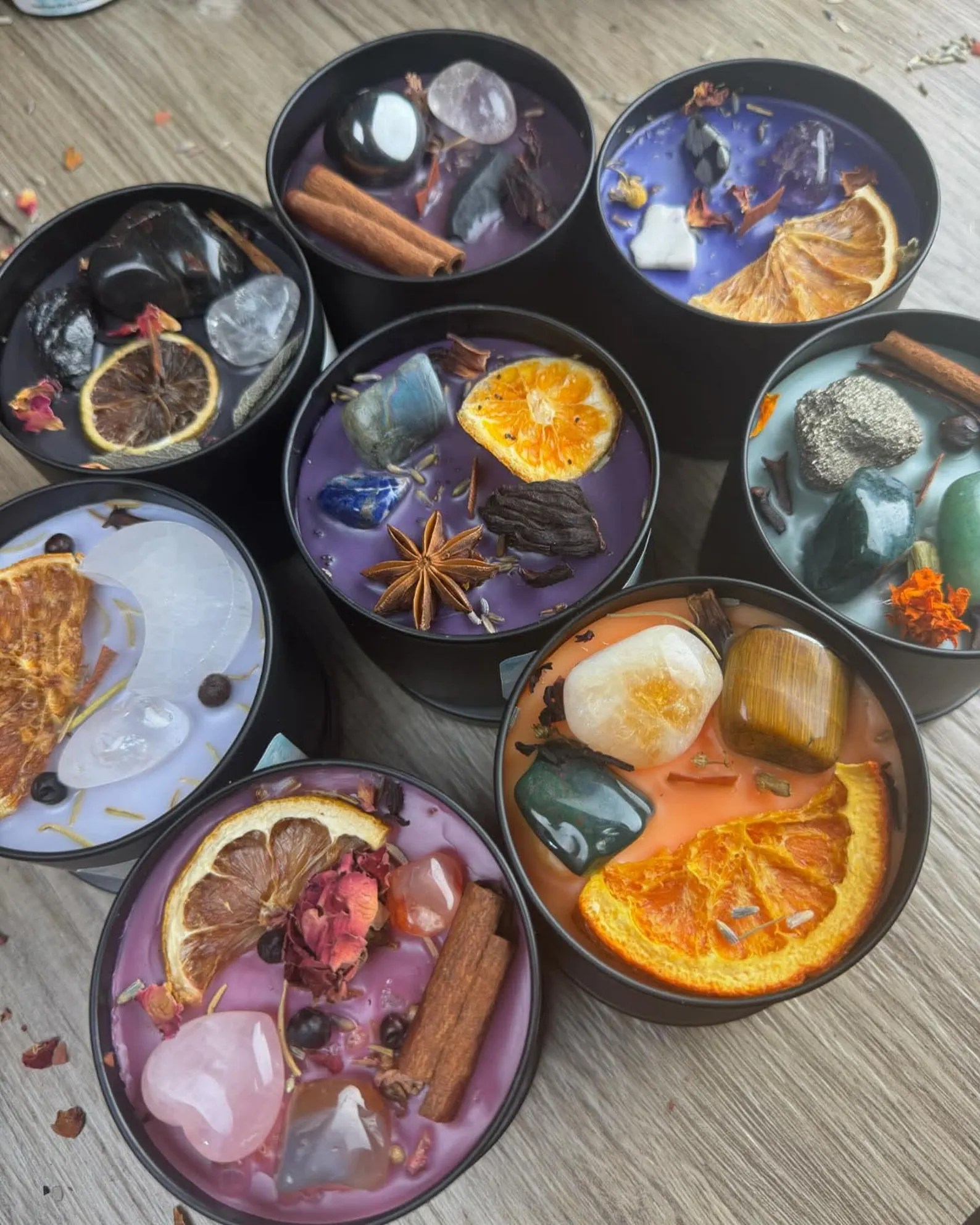 Several round black bowls filled with colorful wax and floating dried fruits, spices, and petals (purple, pink, orange) used as scented candles or potpourri potpourri centerpieces.