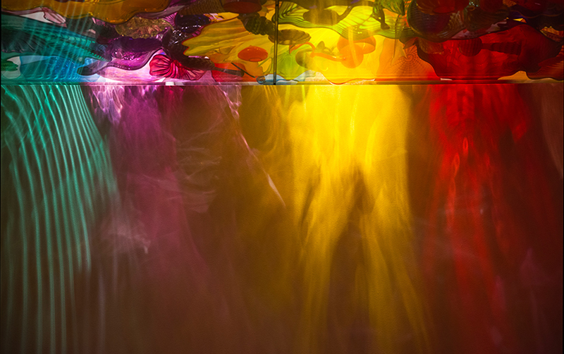 This abstract glass art canvas print transforms glowing reds, golds, purples and turquoise into streams of light that seem to flow through the image. Reflections and refractions blur the line between glass and water, giving the photograph an almost liquid quality.