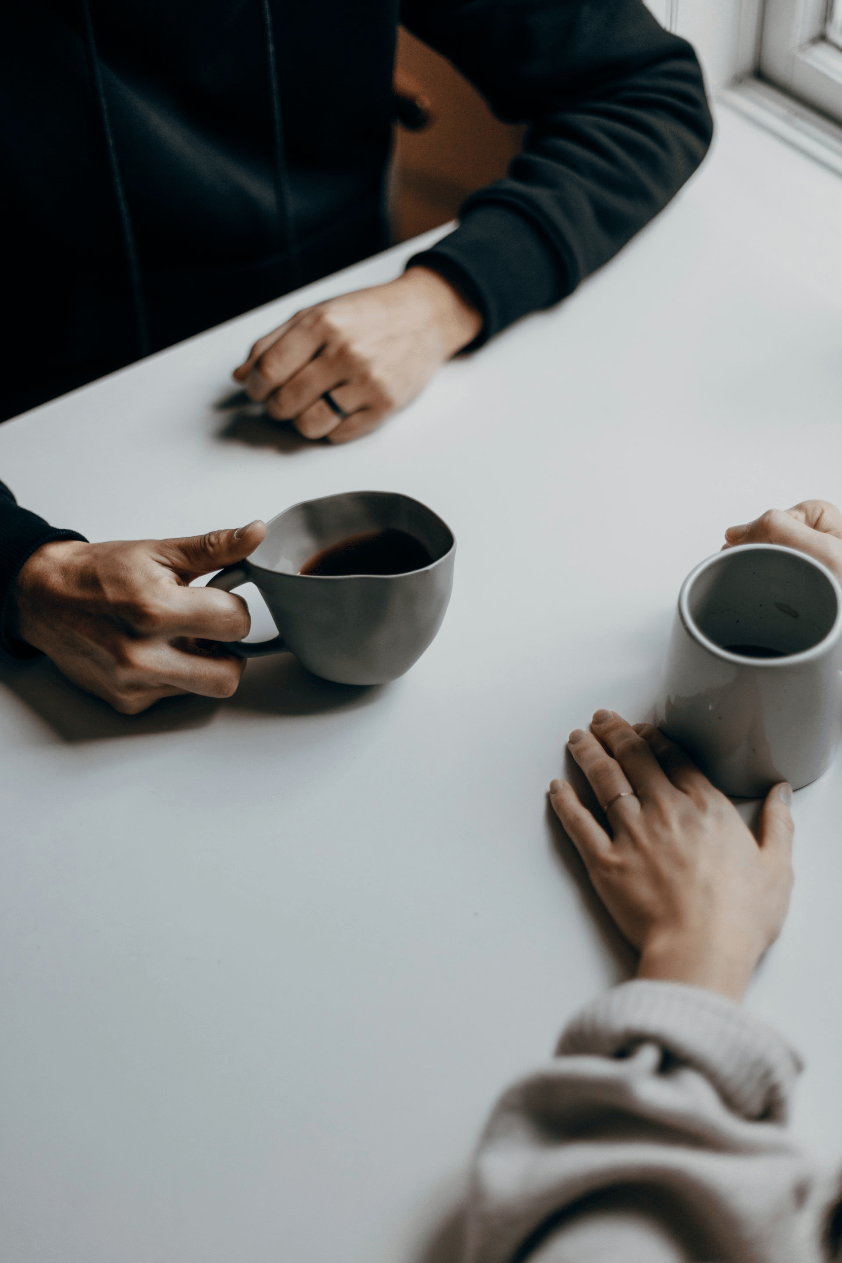 Two people sitting at a table talking over cups of coffee
