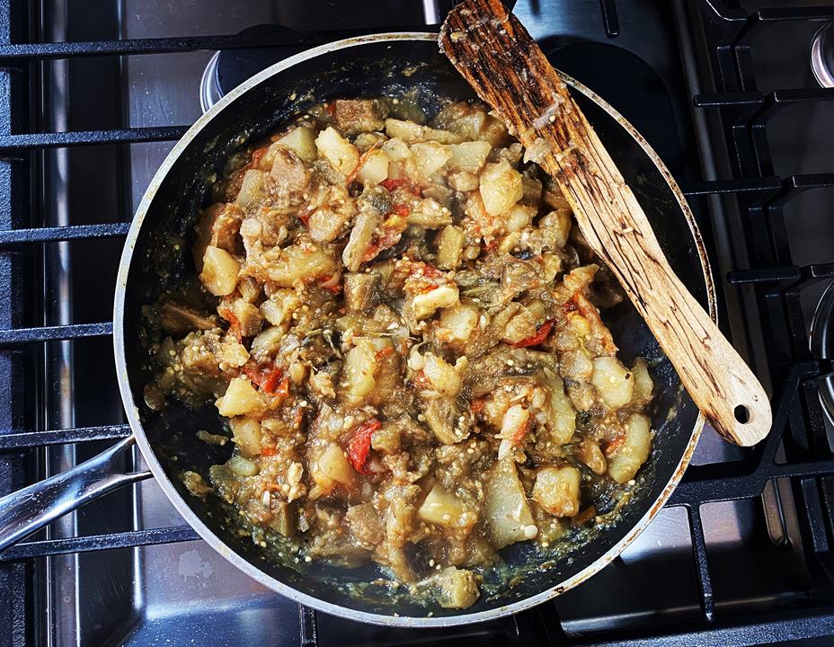 Eggplant and potato dish in a pan on the stove with a wooden spoon resting on top