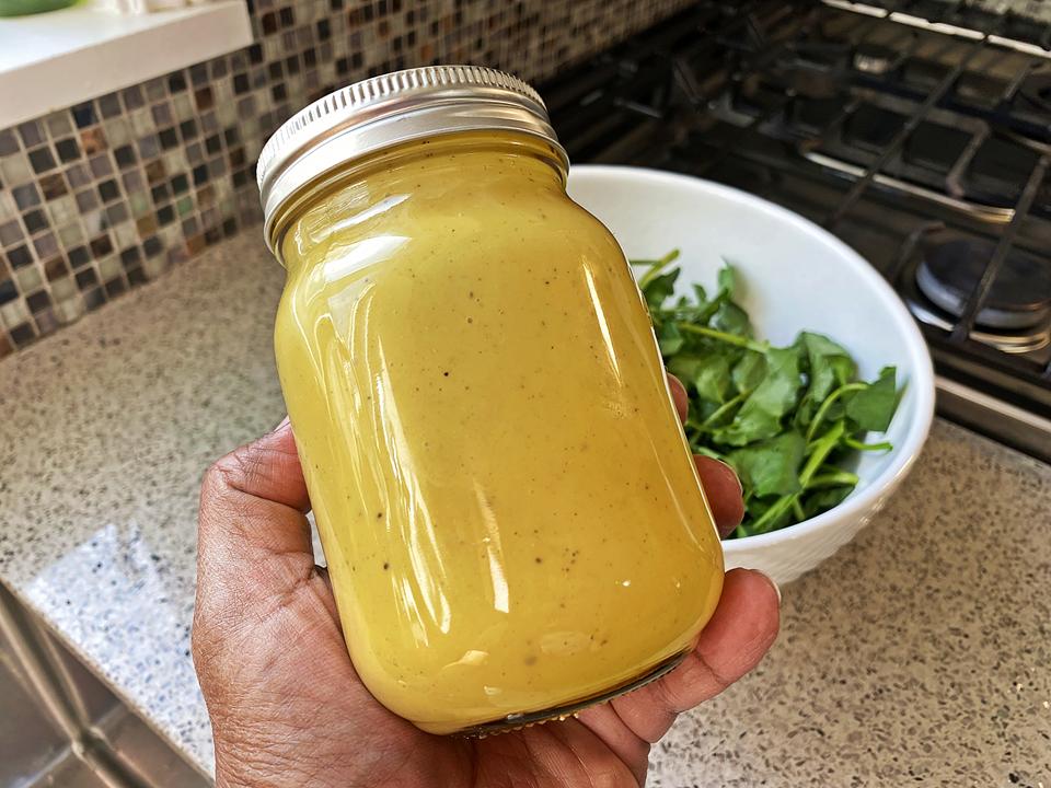 Honey mustard dip in a closed jar with greens in a white bowl in the background