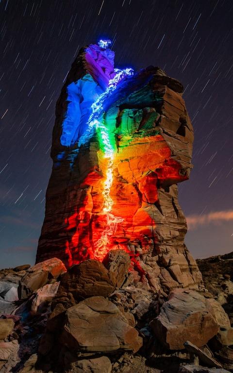 Luke Rasmussen climbing a rock tower in Page, Arizona,, USA wearing LED lights as to make a rainbow effect on the side of the rock face. See SWNS copy SWCAclimb: These fascinating images show a climber turning his route into a rainbow as he scales sheer rocks while wearing LED lights. Luke Rasmussen takes to sky-high ridges across the USA under the cover of darkness, tracking his journeys with colourful patterns. He records the routes through a series of long exposure images taken from the foot of each rock face.
