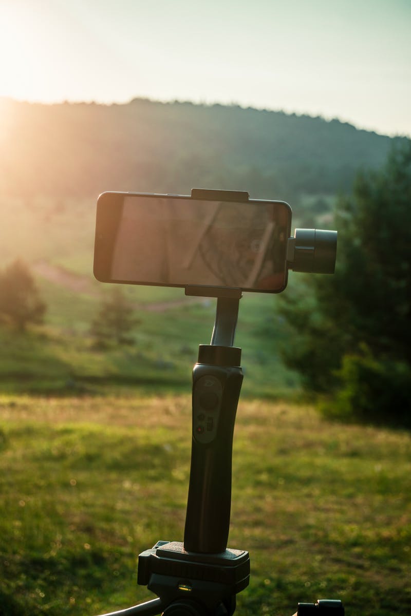 A smartphone mounted on a gimbal capturing a scenic sunset view of a green landscape.