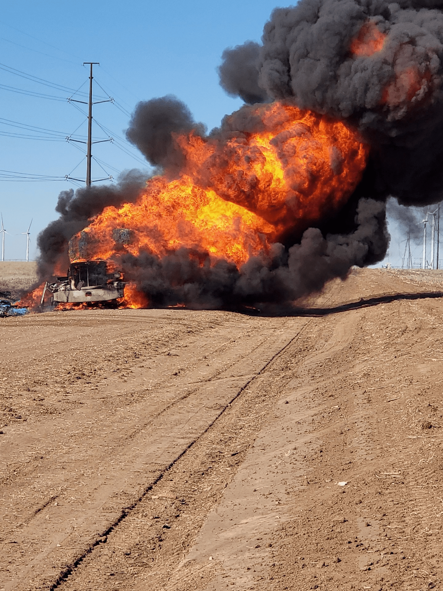 A car on the side of the road on fire burning creating dark smoke.