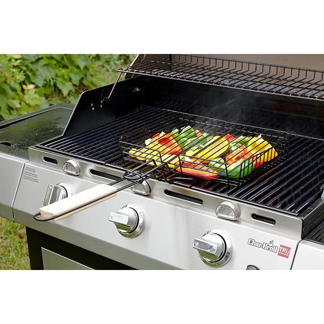 Grilling basket filled with skewered vegetables on a gas grill, emitting smoke.