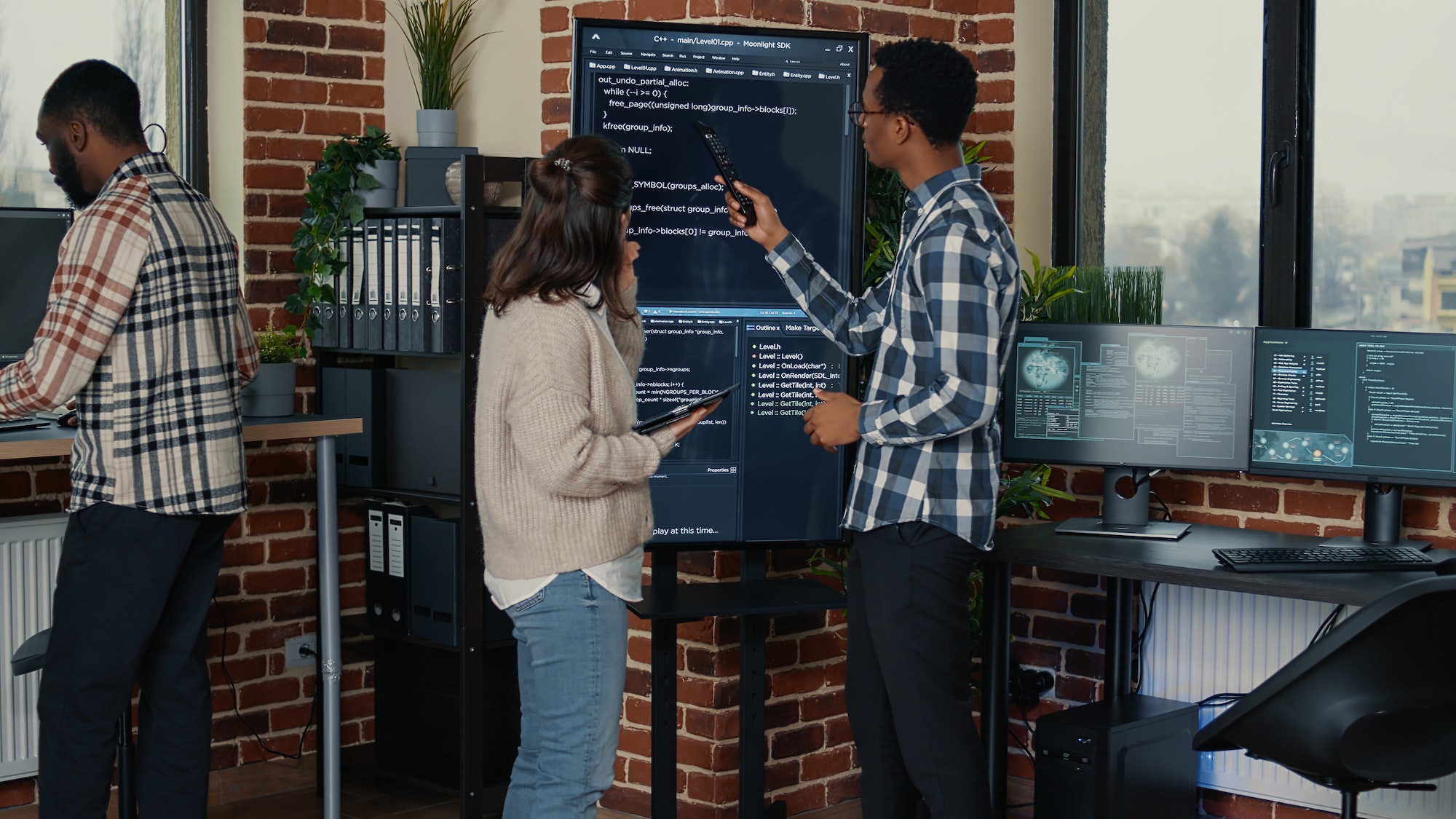 Team of database admins analyzing source code on wall screen tv comparing errors using tablet